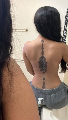 a woman with a tattoo on her back is looking at herself in the bathroom mirror