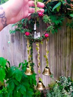 a hand is holding a small christmas wreath with bells hanging from it's side