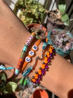 two bracelets with numbers and beads on each one hand, in front of potted plants