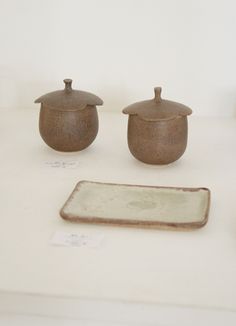 three pots and a plate on a white counter top with tags in front of them