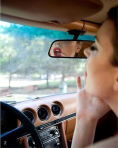 a woman is sitting in the driver's seat of a car looking at her reflection