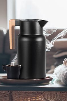 a black coffee pot sitting on top of a table next to a cup