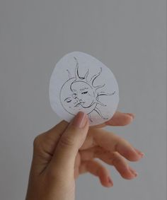 a hand holding a piece of paper with a drawing of a sun and a face on it