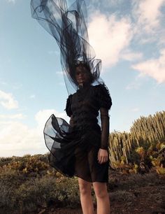 a woman is standing in the desert with her hair blowing in the wind and wearing a black dress