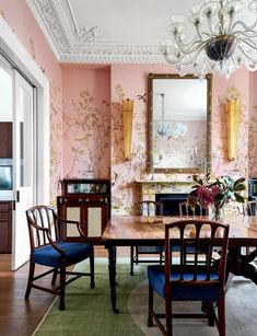 a dining room with pink walls and floral wallpaper on the walls, along with blue upholstered chairs