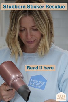 a woman is holding a hair dryer and looking at the label on her shirt