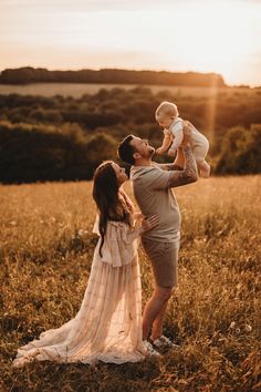 a man holding a baby in his arms while standing next to a woman on top of a field