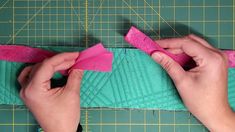 someone is cutting fabric with scissors and a pink piece of cloth next to it on a green surface