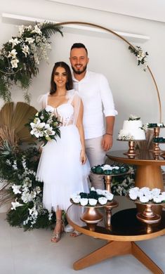 a man and woman standing next to each other in front of a table with cupcakes