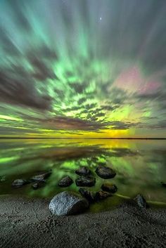 an aurora bore over the ocean with rocks in the foreground