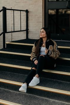 a woman sitting on some steps with her hand in her pocket and looking up at the sky