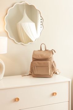 a purse sitting on top of a white dresser next to a round mirror and lamp