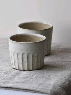 two white ceramic bowls sitting on top of a gray table cloth next to each other