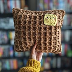 a person holding up a brown knitted pillow with a smiley face on the front