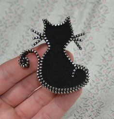 a hand holding a small black cat brooch with beads on it's back