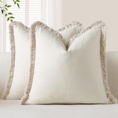 two white pillows with ruffled edges sit on a couch next to a potted plant