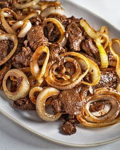 a white plate topped with beef and onions next to onion rings on top of a table