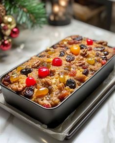 a pan filled with fruit and nuts on top of a table next to a christmas tree