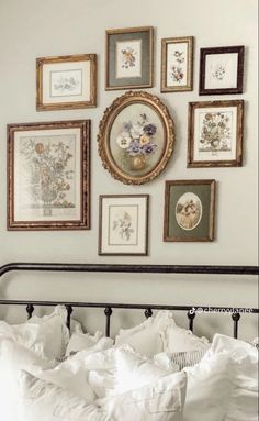 a bed with white linens and framed pictures on the wall above it, in front of a metal headboard