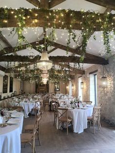 the dining room is set up with white linens and greenery hanging from the ceiling