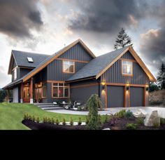 a large gray house sitting on top of a lush green field next to a forest