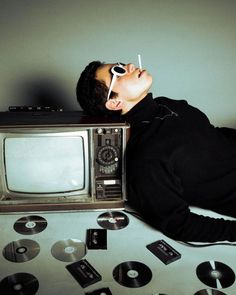 a man laying on top of a table next to an old tv and cd's