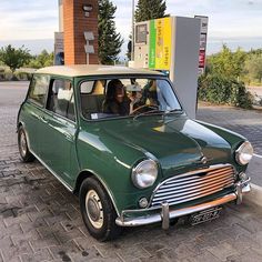 an old green car parked in front of a gas station with a woman driving it