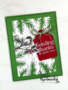 a handmade christmas card with a bird holding a red tag and pine branches on it