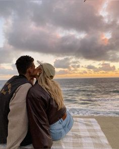 a man and woman sitting on top of a beach next to the ocean under a cloudy sky