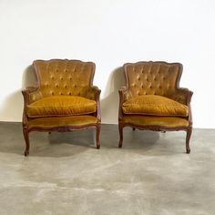 two brown chairs sitting next to each other on cement floored area with white walls