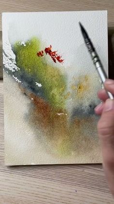 a person is holding a paintbrush in their left hand and painting on a piece of paper