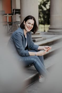 a woman sitting on the steps in front of some pillars and smiling at the camera