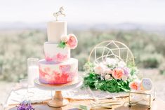 a wedding cake sitting on top of a wooden table next to flowers and greenery