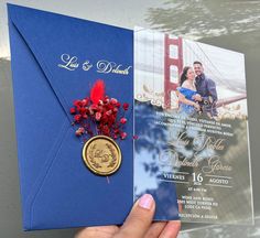 a person holding up a wedding card with a golden seal on it and red flowers