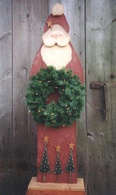 a christmas decoration with a santa clause on top and evergreen wreath around the base, in front of a wooden fence