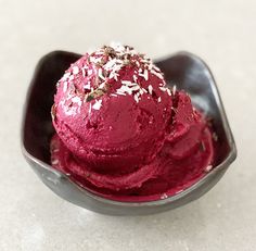 a scoop of red ice cream with sprinkles on top in a black bowl