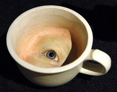 a close up of a white cup on a black surface with an eye in it