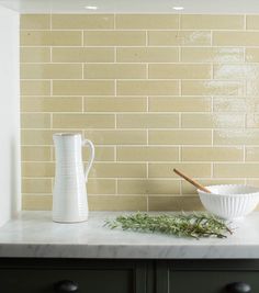 a white vase sitting on top of a counter next to a bowl filled with greens