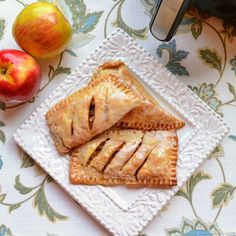 three pastries on a white plate next to apples