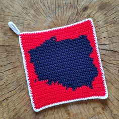 a crocheted red and blue square on top of a wooden table next to a piece of wood