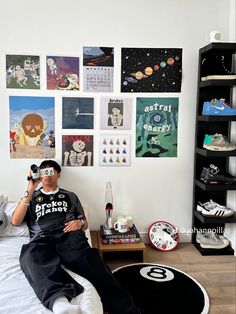 a man sitting on top of a bed in front of a wall covered with pictures