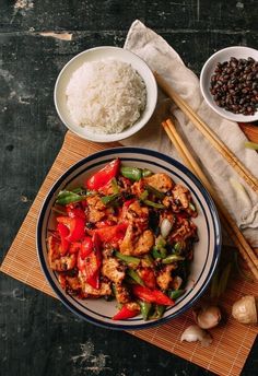 a plate with chicken, peppers and rice on it next to chopsticks in bowls