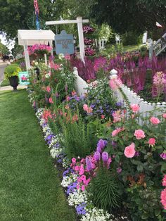 a garden filled with lots of flowers next to a white picket fence on top of a lush green field