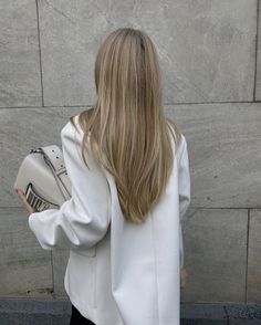 a woman with long blonde hair is holding a white purse and looking at the wall