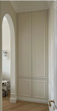 an arched doorway leading to a bedroom with white walls and wood flooring, along with built - in closets