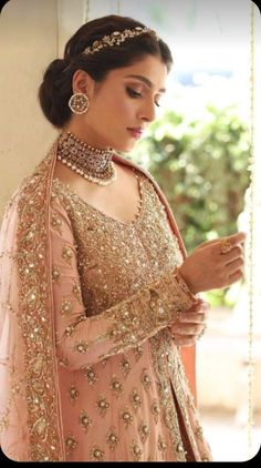 a woman in a pink lehenga and gold jewelry is looking at her cell phone