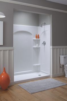 a bathroom with a shower, toilet and rugs on the wooden floor in front of it