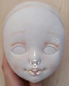 someone is holding up a white doll with eyes and nose patches on it's face