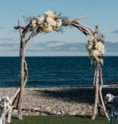 a wooden arch decorated with white flowers and greenery on the grass by the ocean