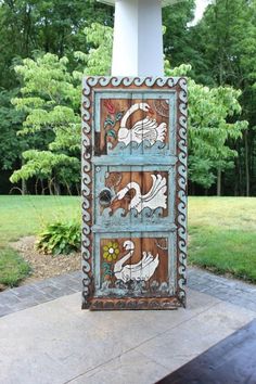 an old wooden door with swans painted on the front and side panels, sitting in a garden